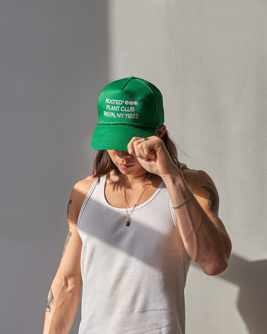 A man wearing the Rooted Plant Club Trucker Hat in green.